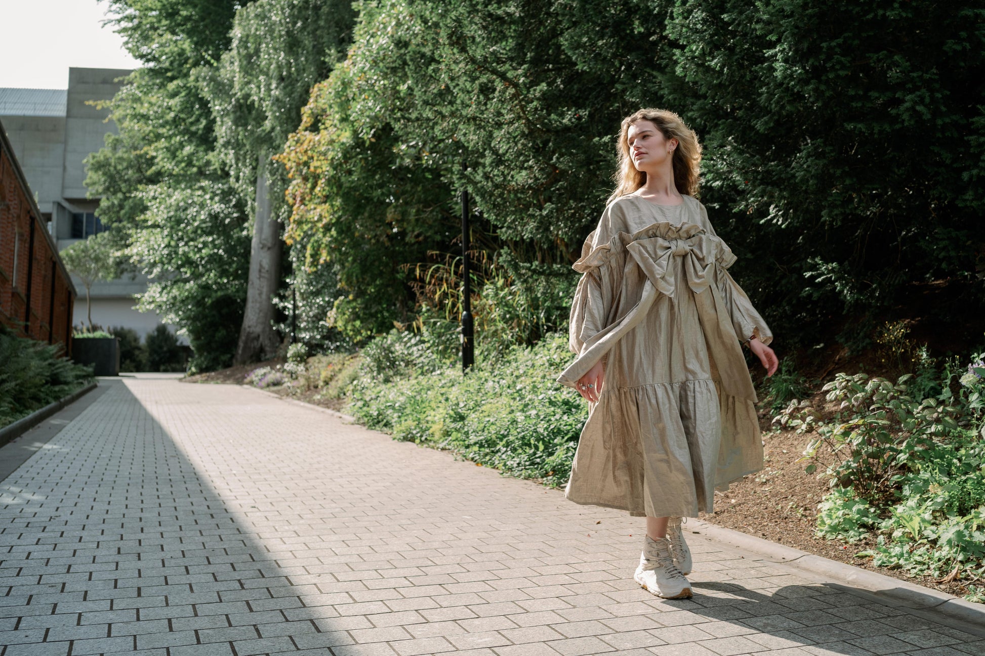 BOW DRESS | A new shape for AW23, The Bow Dress is one of our most playful. The dress is an oversized shape with gathered tiered details. The frill and bow detail at the front is the show-stopper. We have created this one in a beige/gold beetled linen whi