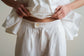 Close view of a white blouse and skirt with gathered waist and button fastening, highlighting drape and soft texture.