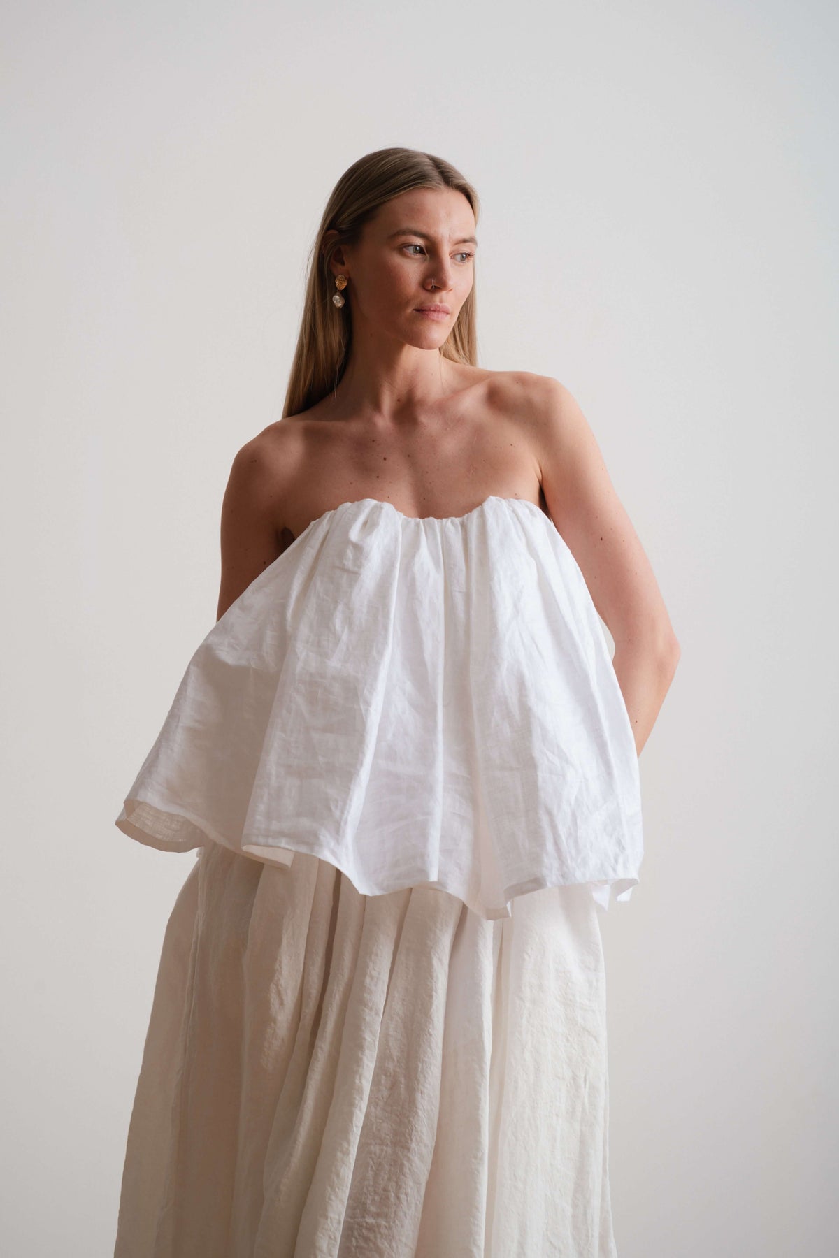 Model wearing a strapless white top with gathered volume and a flowing skirt, shown against a neutral backdrop.