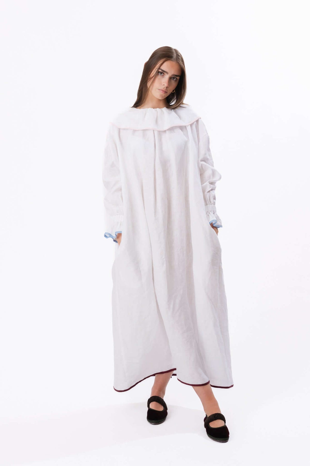 Loose white dress with wide neckline and long sleeves, photographed full length to show drape and shape.