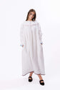 Loose white dress with wide neckline and long sleeves, photographed full length to show drape and shape.