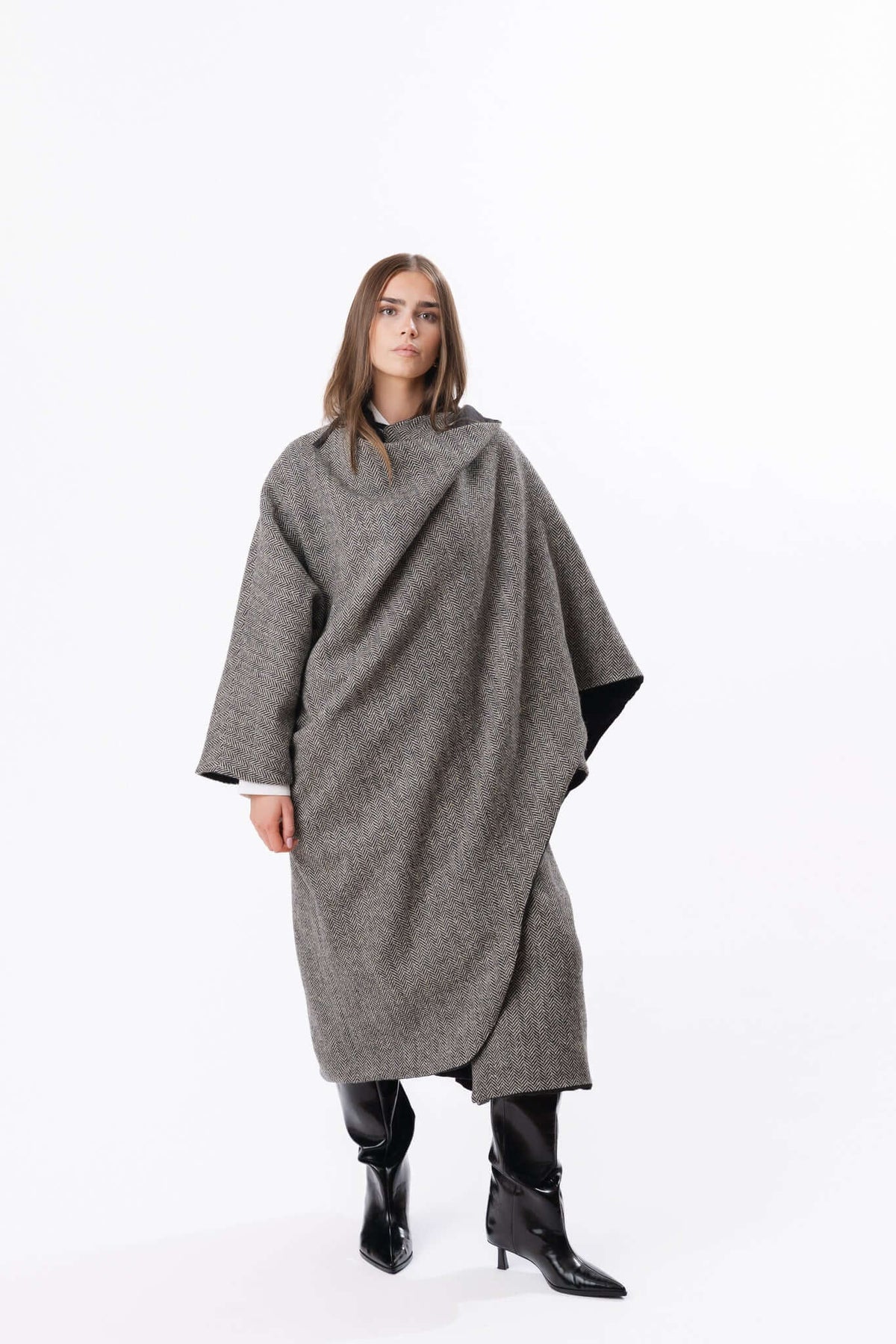 Grey cocoon-style cape dress worn with black boots, shown full length against a clean studio backdrop.