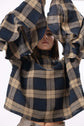 Close view of a checked dress with oversized sleeves raised overhead, highlighting structure, scale and movement.