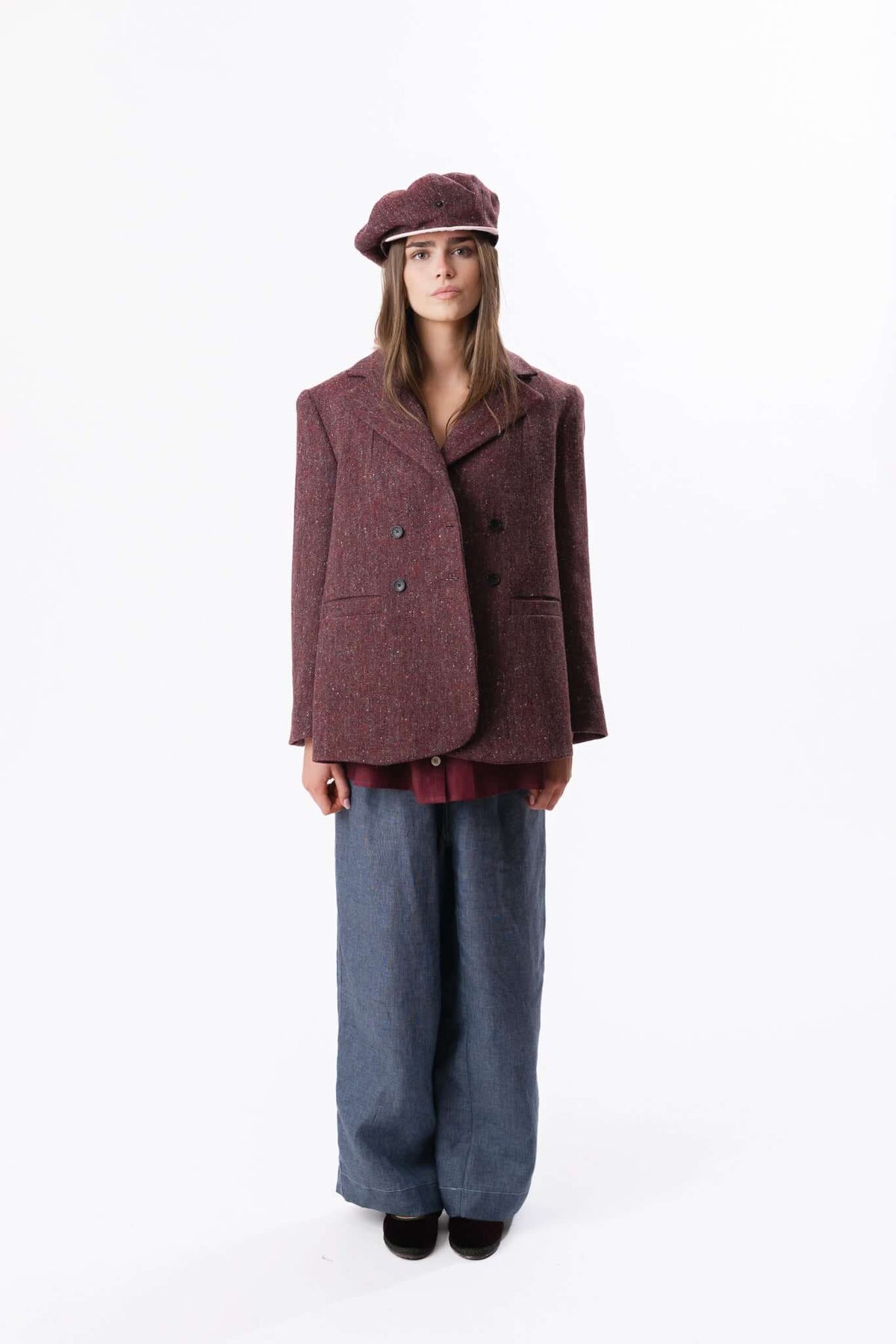 Model wearing a textured burgundy jacket, matching cap and wide trousers against a neutral studio backdrop.