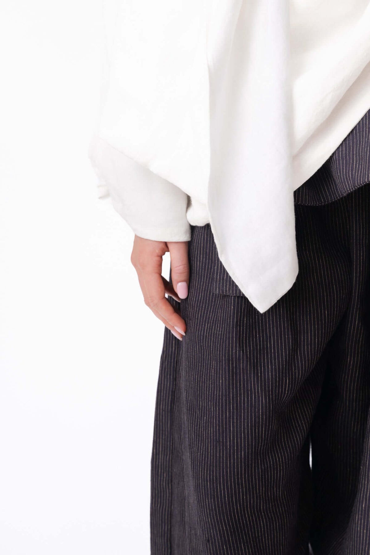Close view of a white blouse and dark skirt, focusing on the drape of the sleeve and hand detail in the studio.