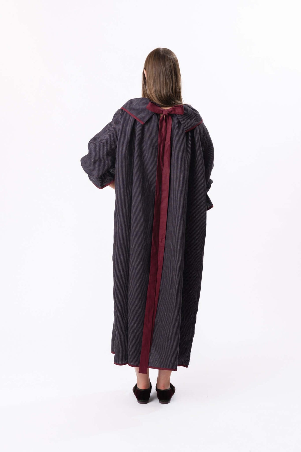 Back view of a long dark coat with contrasting central panel, shown full length in a studio setting.