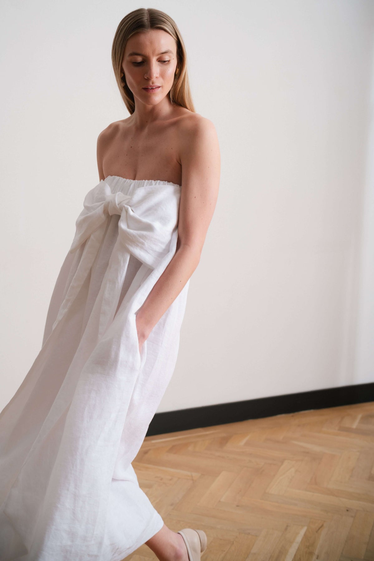 Model in a strapless white dress turning slightly to show gathered volume and soft movement of the fabric.
