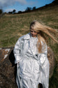 Woman wearing a silver-toned coat outdoors on rocks, captured with wind through the hair and fabric.