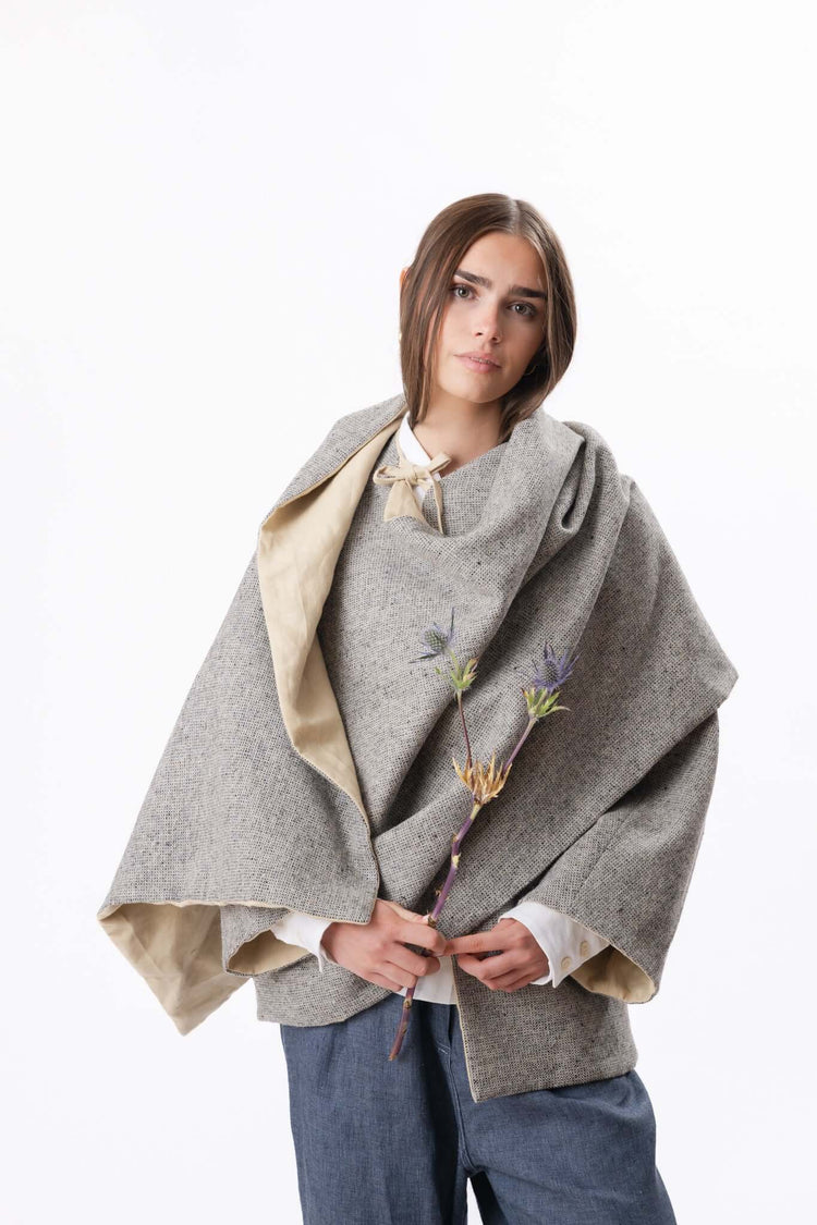 Model wearing a grey shawl layered over a shirt and trousers, shown front on in a clean studio setting.