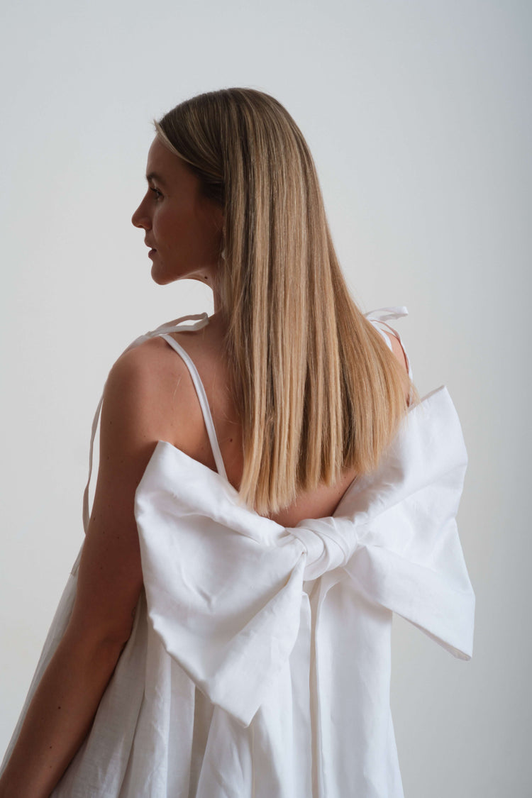 Back view of a sleeveless cream dress with oversized bow detail, highlighting open back and clean lines.