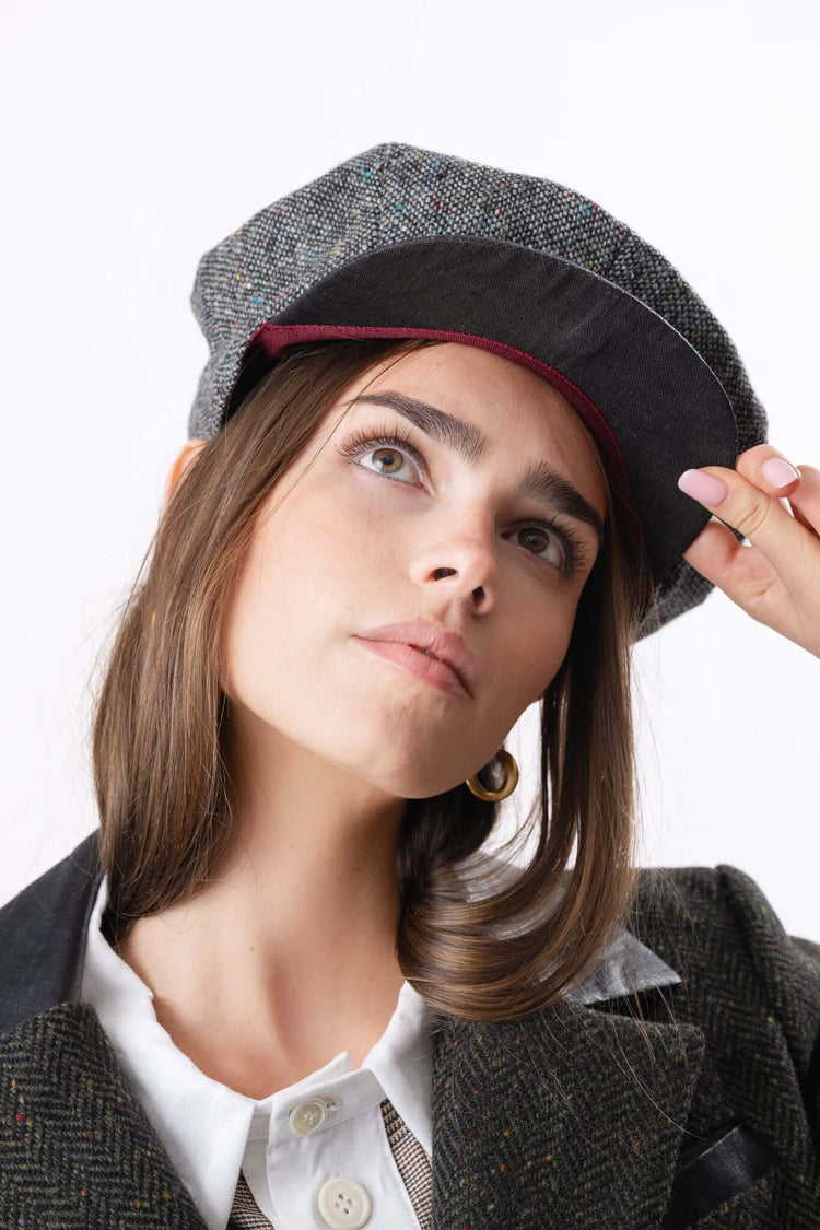 Portrait of a woman in a dark cap and tailored jacket, photographed against a clean studio background.