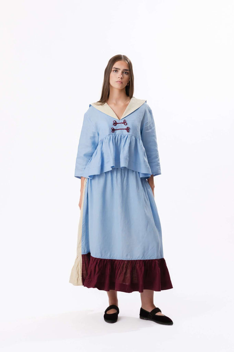 Pale blue dress with wide collar and dark ruffle hem, shown full length against a neutral studio backdrop.