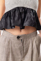 Close detail of a black peplum top and checked trousers, focusing on silhouette, texture and waistline.
