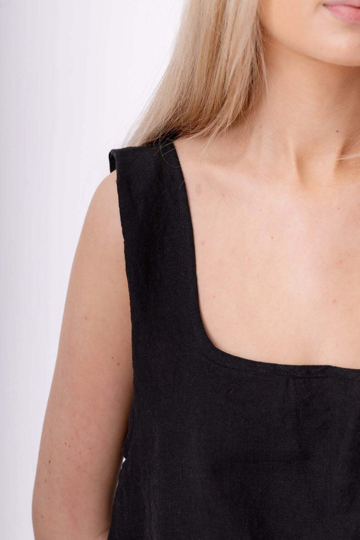 Close detail of a black sleeveless top, cropped at the neckline to show texture, cut, fit and clean finish.
