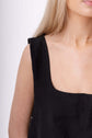 Close detail of a black sleeveless top, cropped at the neckline to show texture, cut, fit and clean finish.