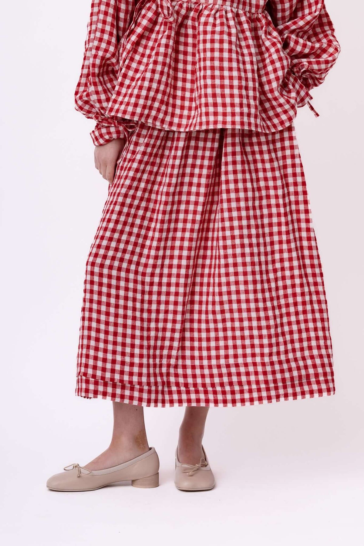 Close view of a red gingham skirt and blouse set, cropped to highlight the hem, drape and fabric texture.