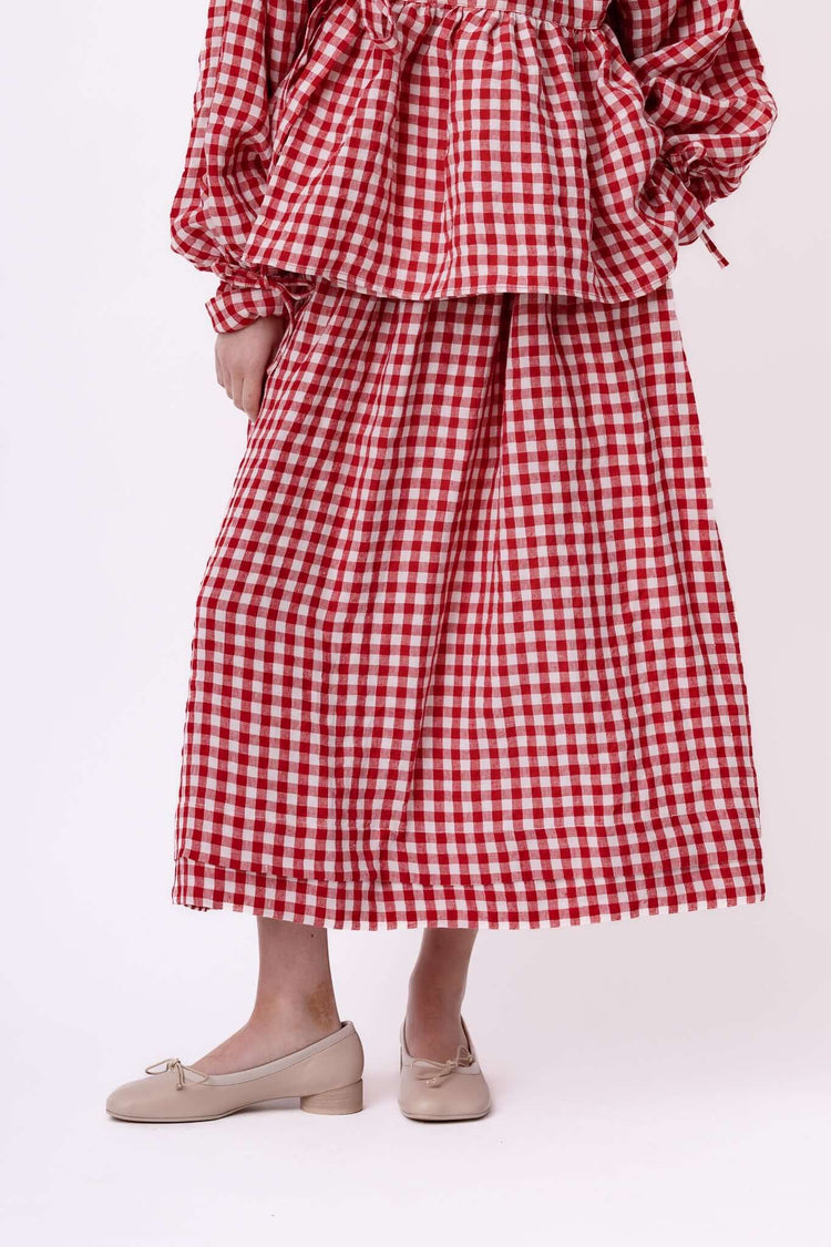 Close view of a red gingham skirt and blouse set, cropped to highlight the hem, drape and fabric texture.