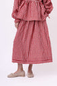 Close view of a red gingham skirt and blouse set, cropped to highlight the hem, drape and fabric texture.