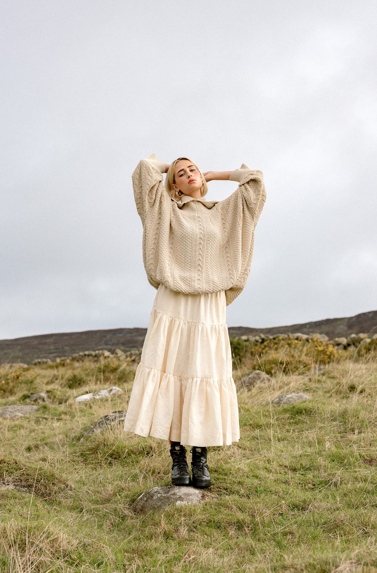 The Kindred Aran jumper worn with a linen skirt on open moorland