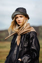 Woman in a dark coat, scarf and cap outdoors, photographed in natural light with wind through the hair.
