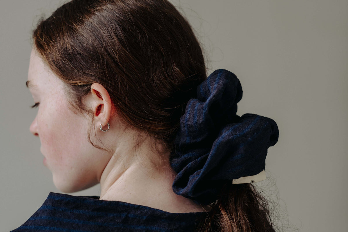 Back view of a dark scrunchie tied around a ponytail, shown close up to highlight colour and texture.