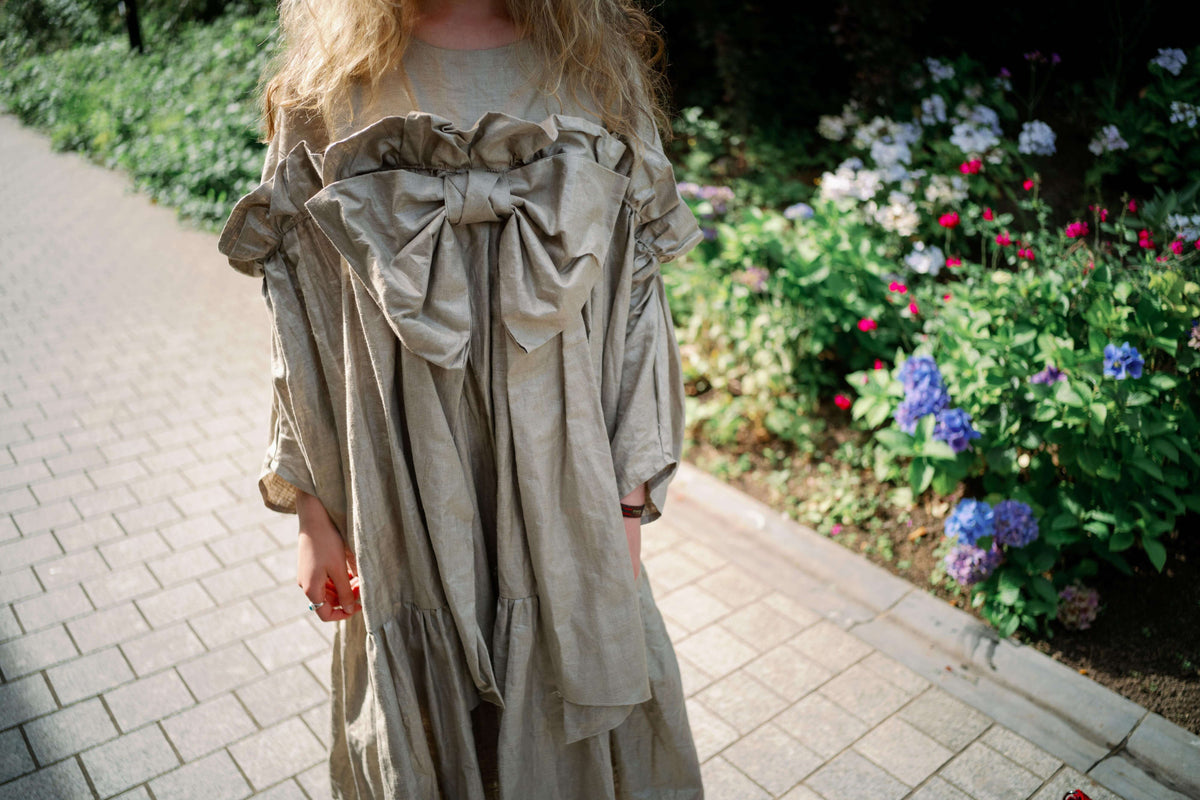 BOW DRESS | A new shape for AW23, The Bow Dress is one of our most playful. The dress is an oversized shape with gathered tiered details. The frill and bow detail at the front is the show-stopper. We have created this one in a beige/gold beetled linen whi