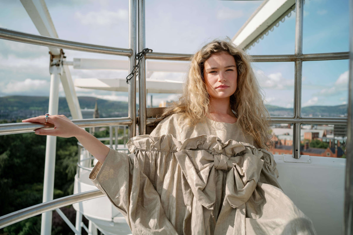 BOW DRESS | A new shape for AW23, The Bow Dress is one of our most playful. The dress is an oversized shape with gathered tiered details. The frill and bow detail at the front is the show-stopper. We have created this one in a beige/gold beetled linen whi