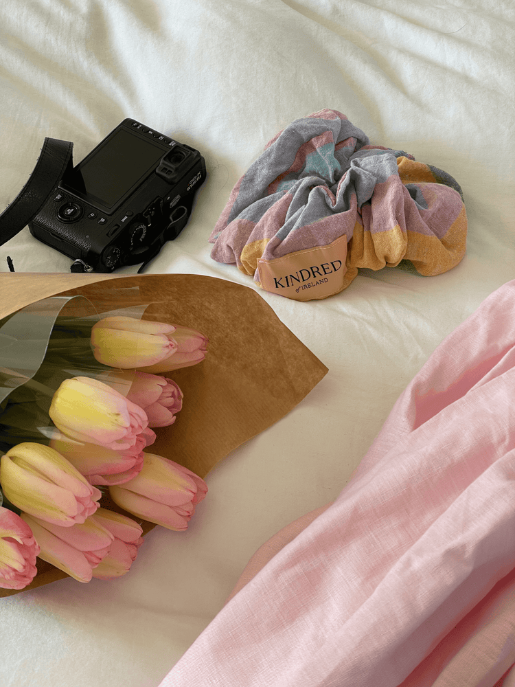 Styled still life with pink tulips, a camera and a pastel scrunchie arranged on cream fabric in soft light.